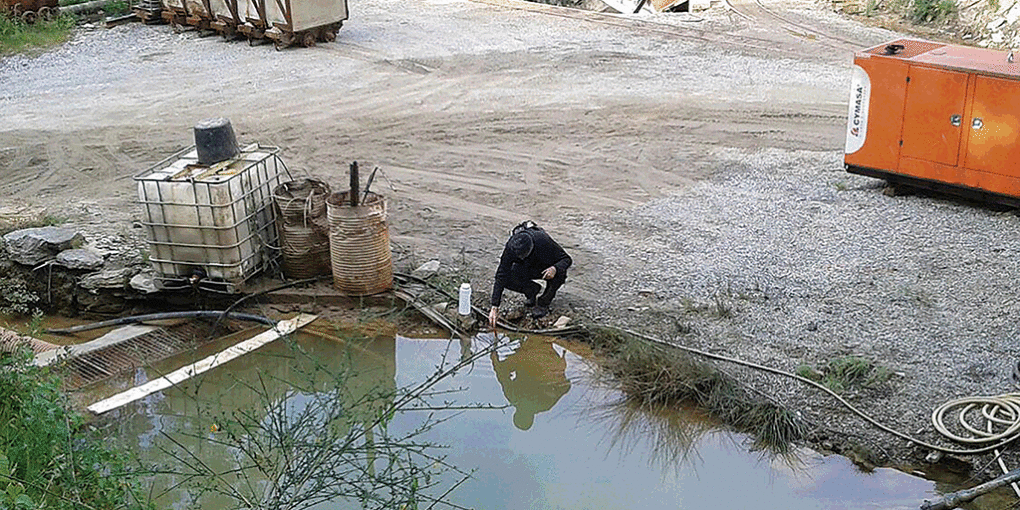 Um ativista da associaçom ecologista Adega recolhe mostras de água numha balsa da mina de Sam Fins.