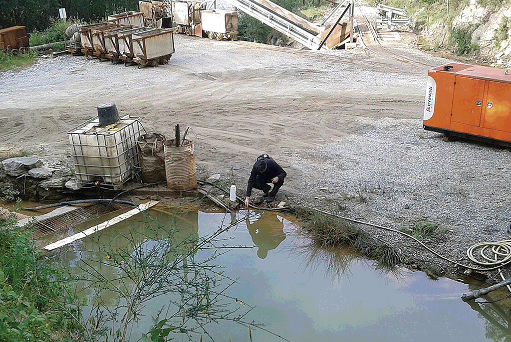 Um ativista da associaçom ecologista Adega recolhe mostras de água numha balsa da mina de Sam Fins.
